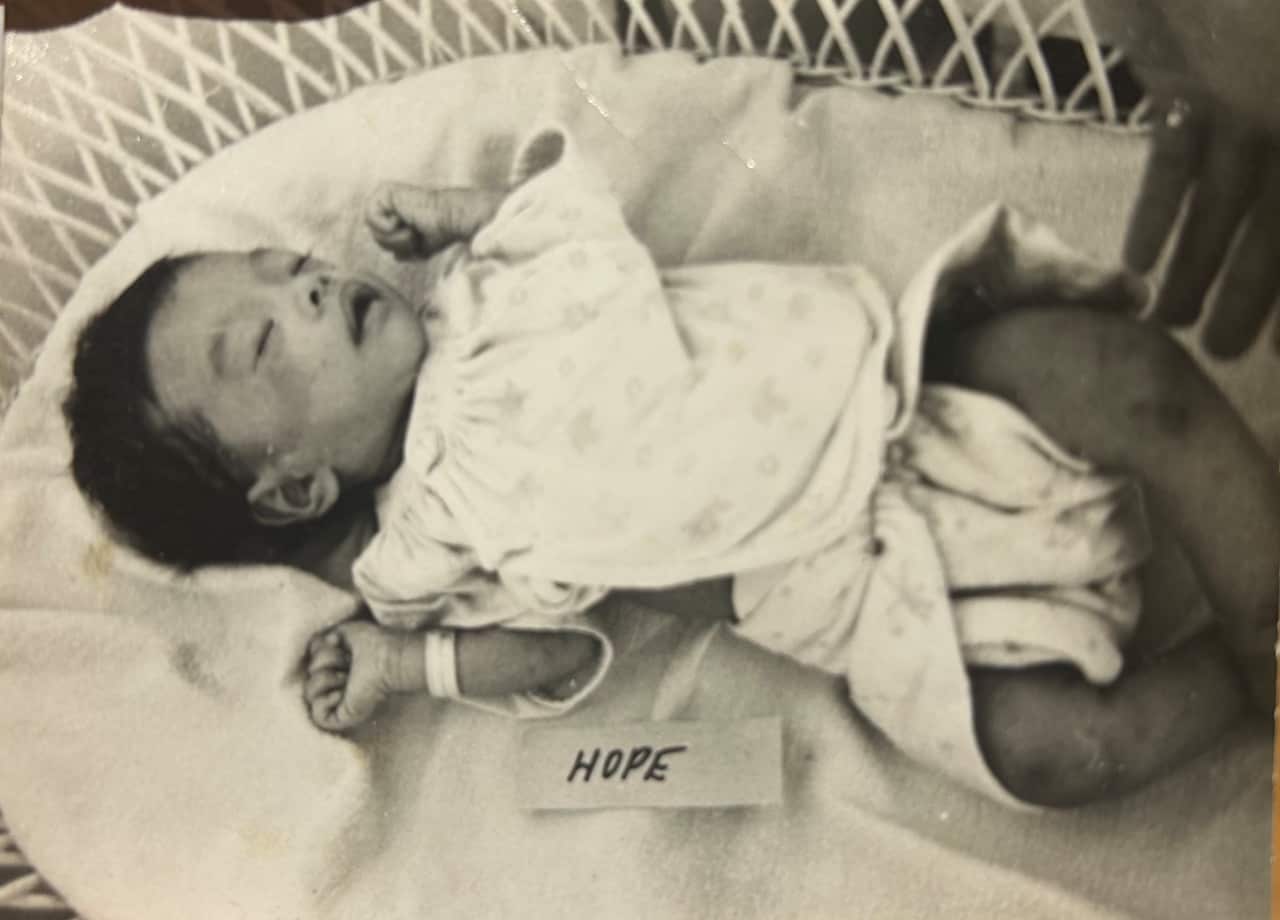 A small baby in a crib, looking malnourished, with a nametag next to her reading 'Hope'.