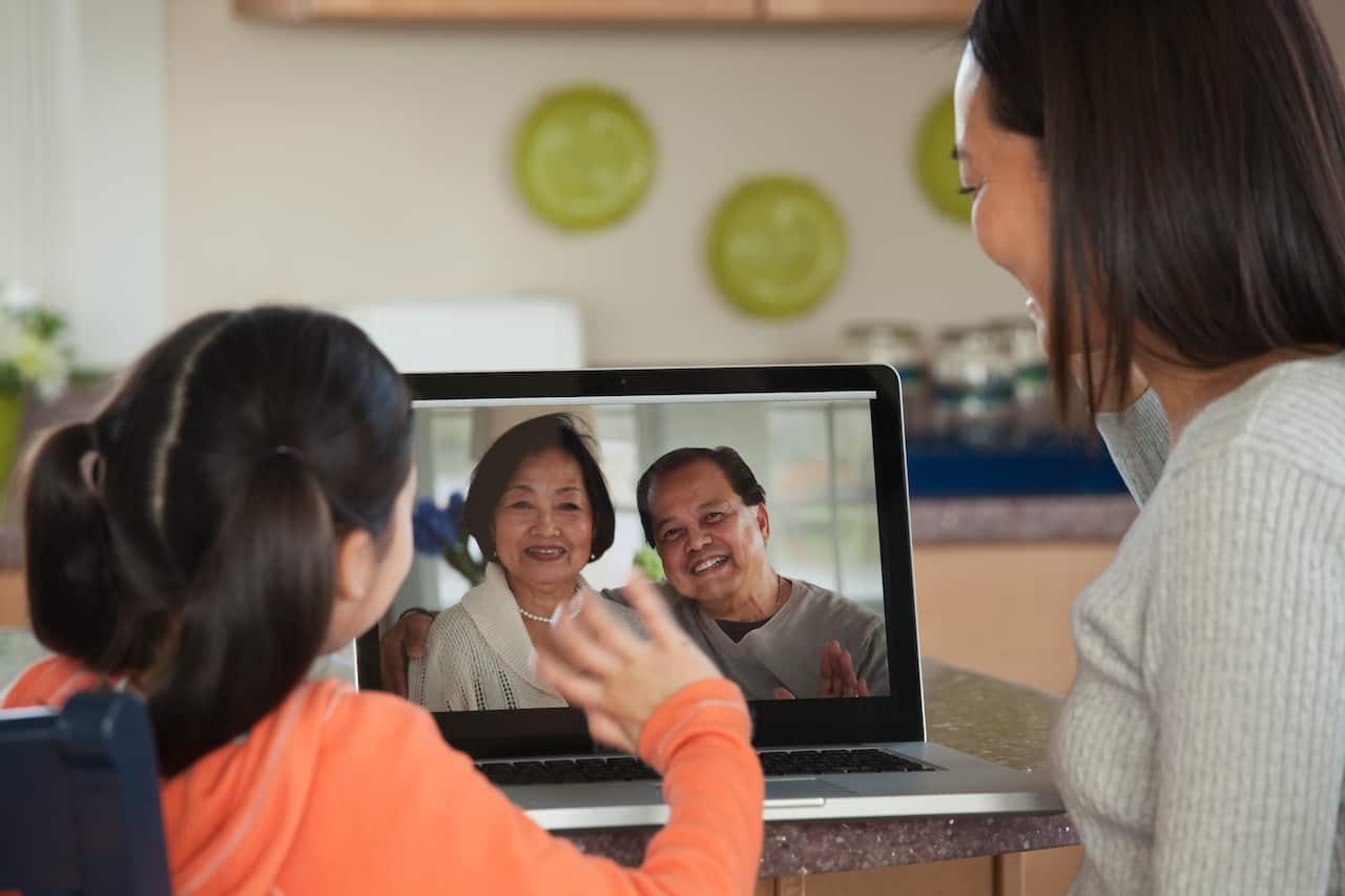 Asian mother and daughter talking to family on laptop