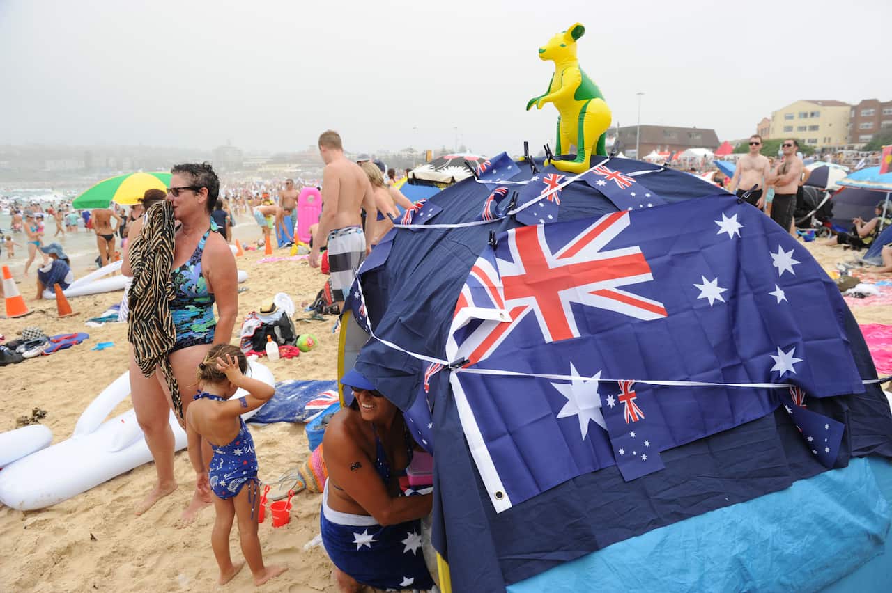 People stand around a tent emblazoned with Australian flags on a beach. 