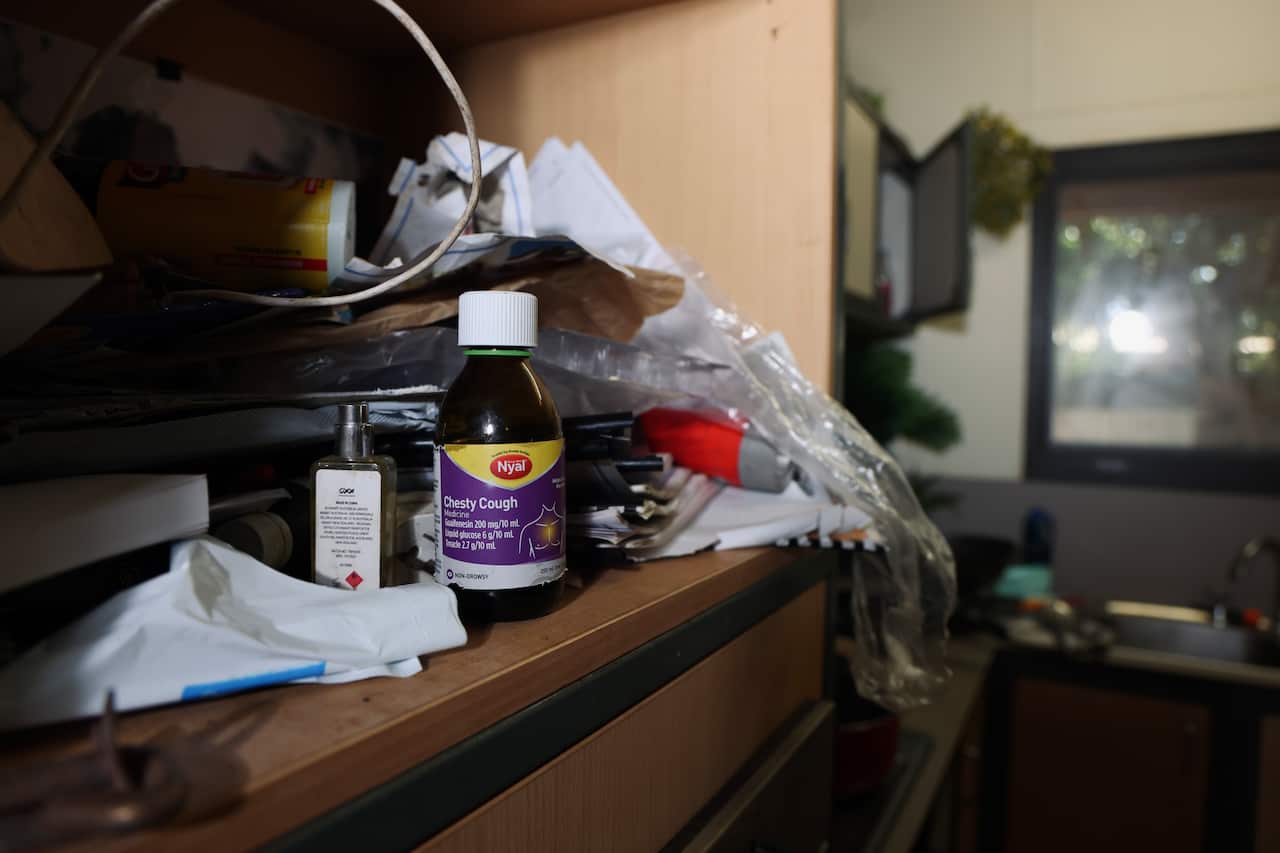 A bottle of cough syrup sits on a shelf in the kitchen among other clutter.