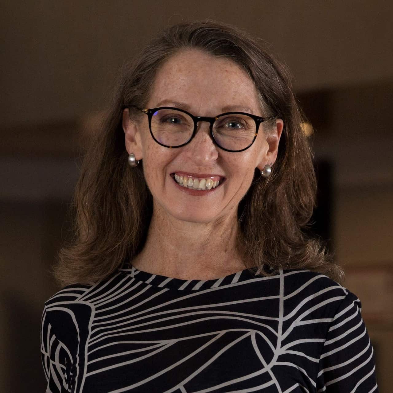 A smiling woman with wavy shoulder-length brown hair and glasses 