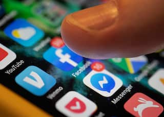 A thumb hovers over a phone screen showing icons including Facebook, Messenger and YouTube.