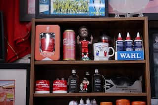 A shelf of Liverpool FC memorabilia, including a figurine of Mohamed Salah, reflects Kleames Dawod's lifelong passion for the club inside his Sydney barbershop.