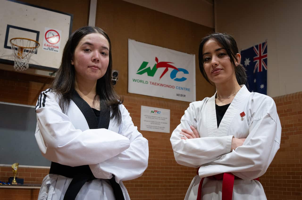 Two women wearing taekwondo uniforms pose for a photo with their arms folded.