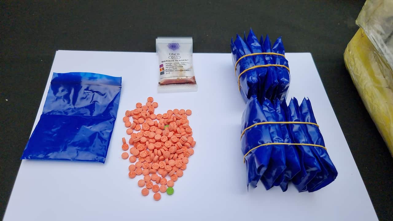 Orange pills on a table with other drugs wrapped up in blue bags.