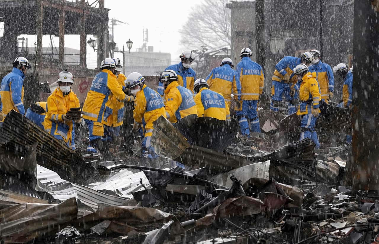 Rain falls as police officers remove the wreckage from a fire.
