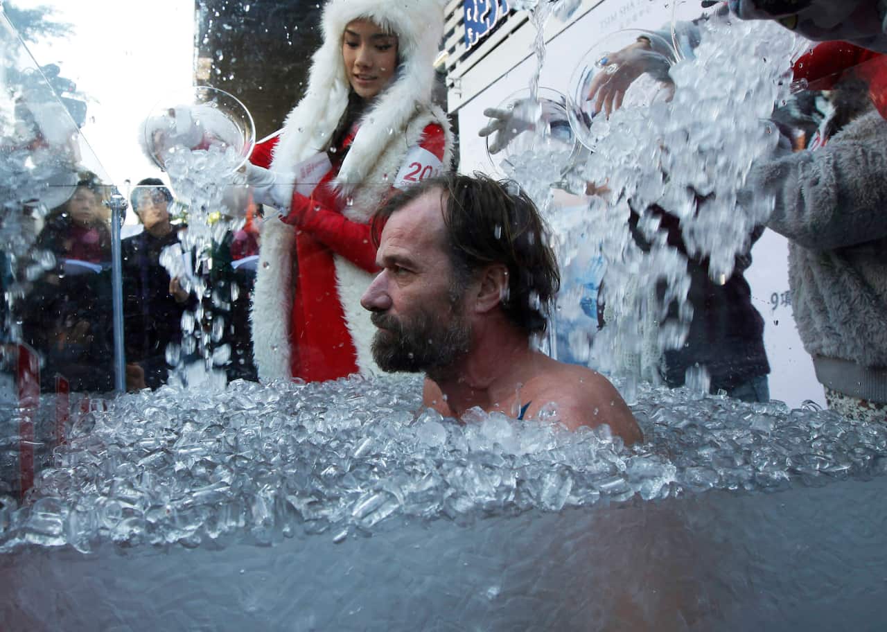A man sits in an ice bath next to a woman wearing a furry white hat.