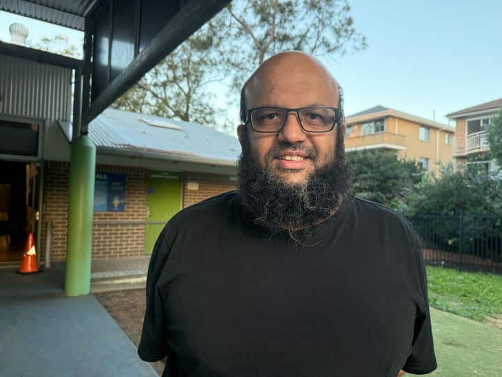 A bearded man with glasses in a black shirt looks forward.
