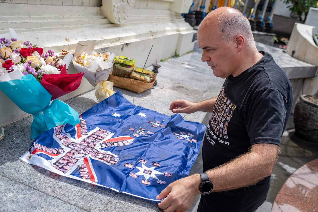 A man lays an Australian flag on steps. The flag features photos of people's faces.