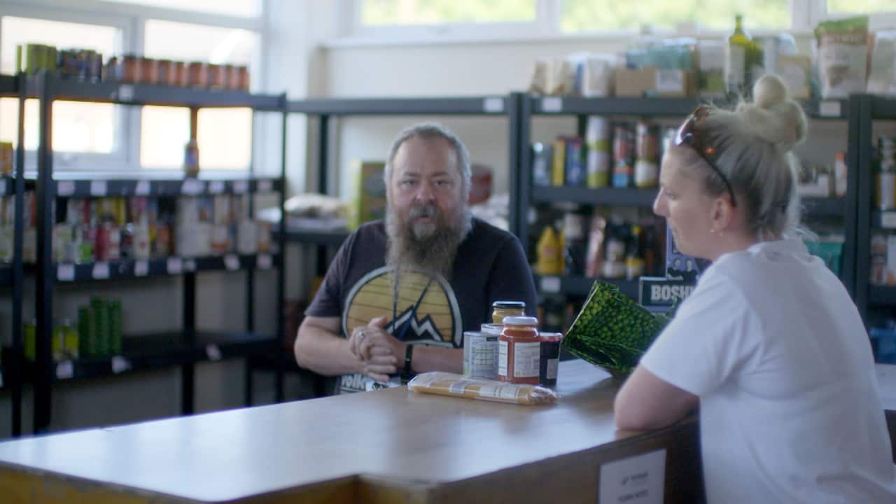 A woman stands at a counter at a food bank opposite a bearded man
