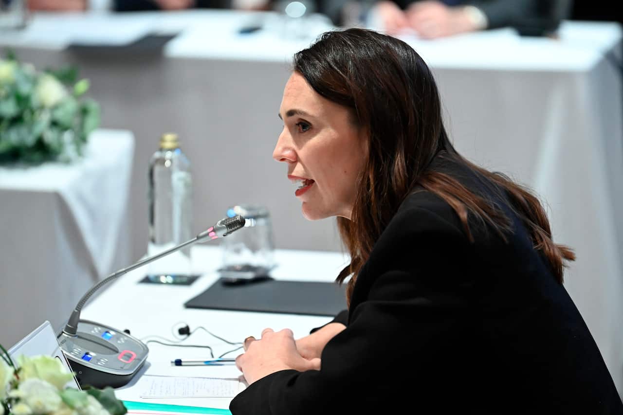 Side profile of Jacinda Ardern speaking into a microphone while sitting at a table.