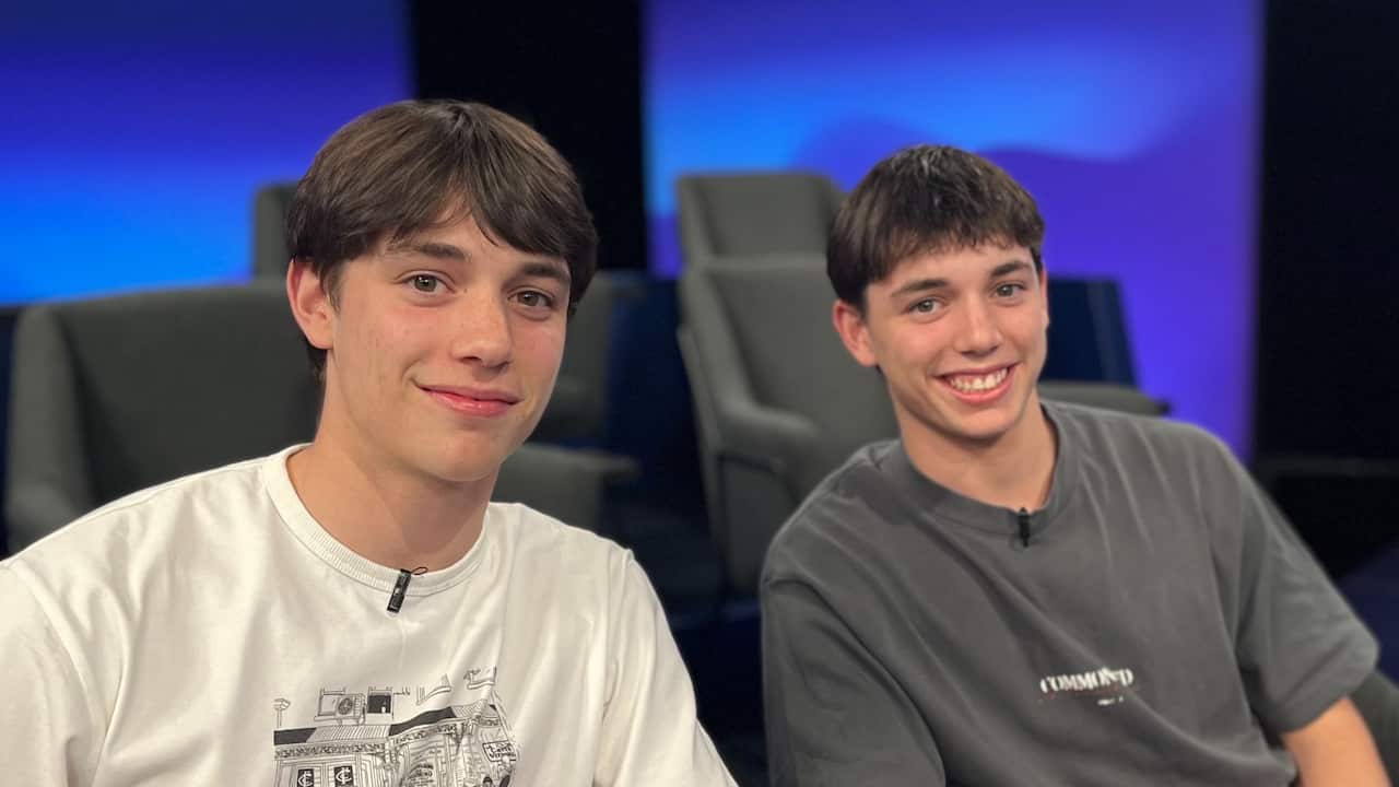closeup of two young male identical twins with brown hair in two shirts in a studio