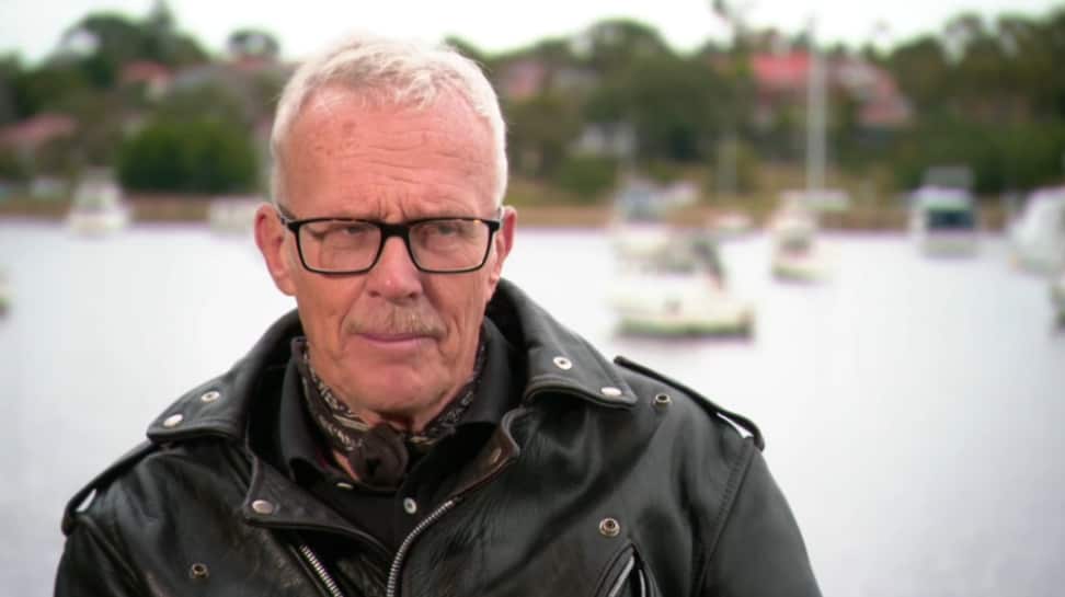A man in a scarf and leather jacket standing in front of a river