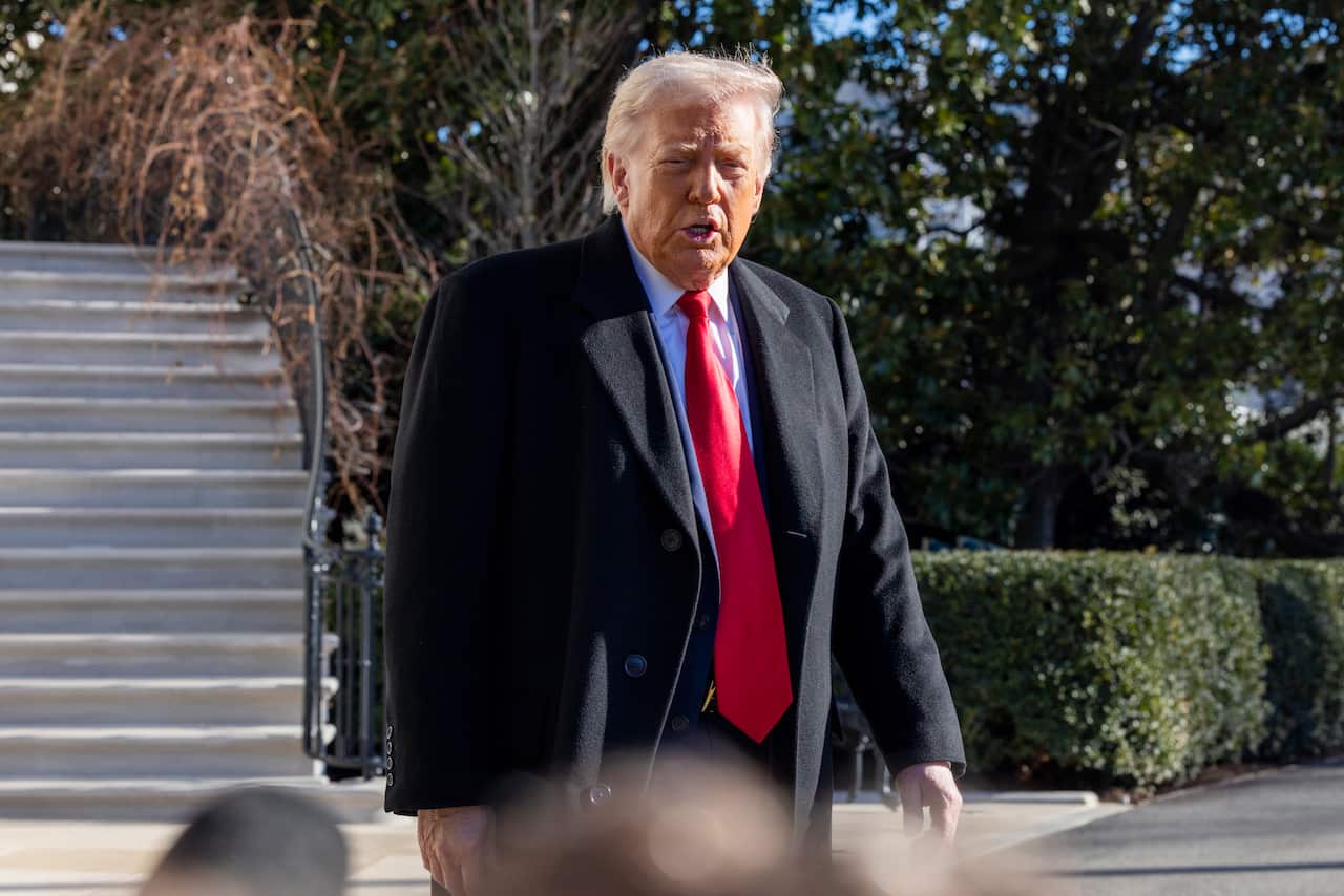 Donald Trump dressed in a black suit and red tie walks near some stairs