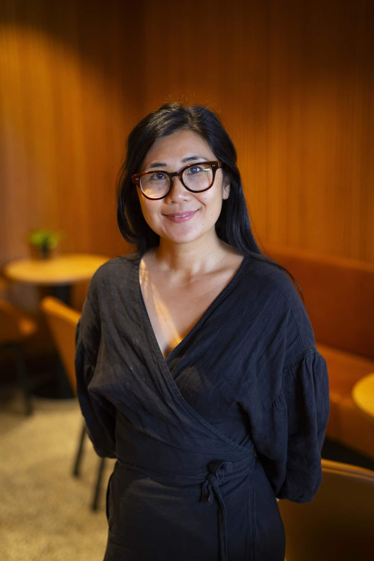 A woman in a black dress and black glasses is smiling.