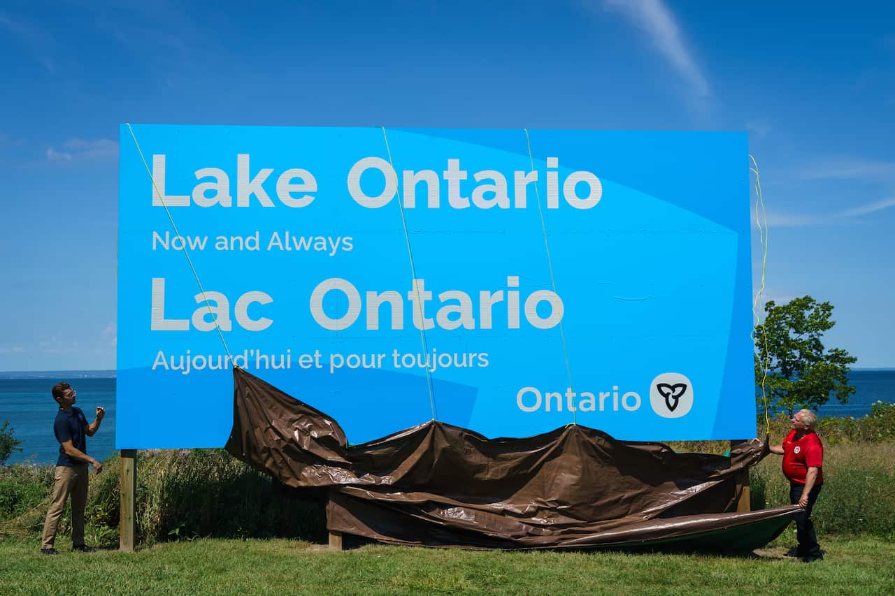 A sign reading Lake Ontario in English and French is unveiled in front of the water.