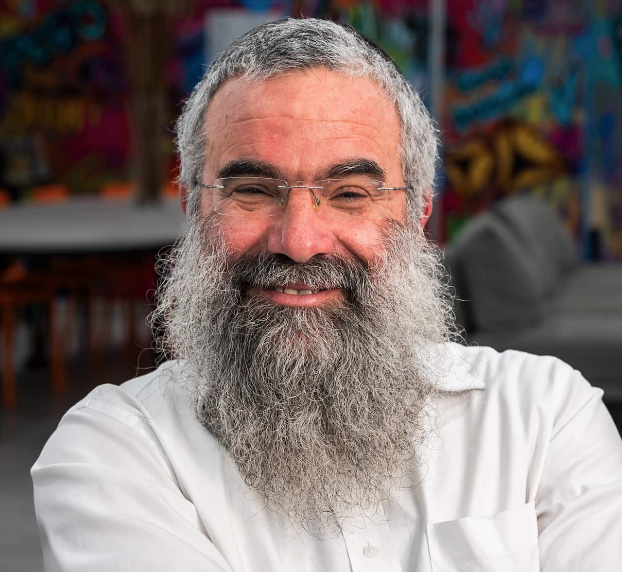 A man with a grey beard sits in front of a colourful mural.
