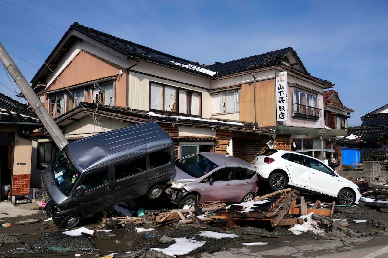 Vehicles and debris are piled up outside a building heavily damaged by an earthquake.