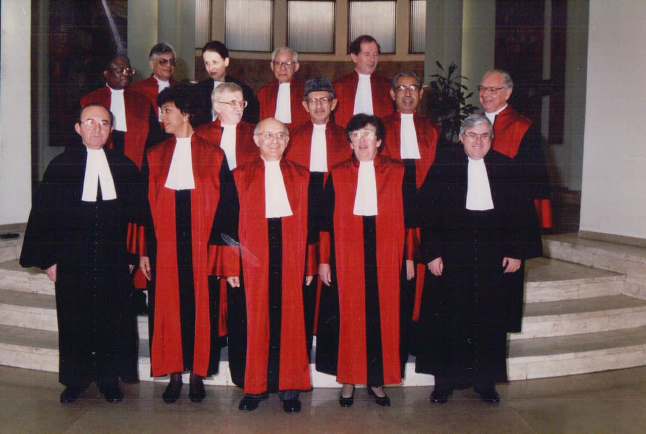 14 people posing for a photo, some wearing red judges robes, standing on white stairs.