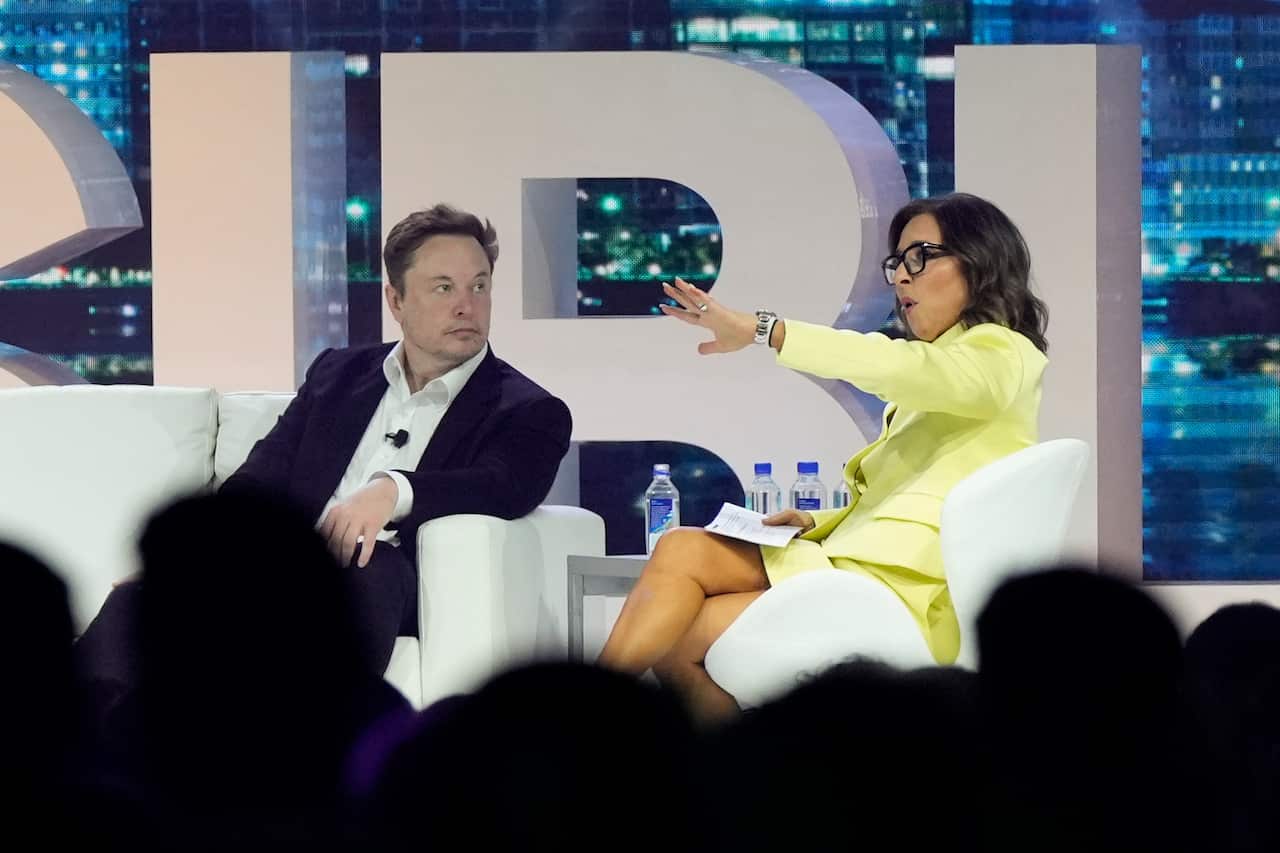 Elon Musk and Linda Yaccarino sitting in chairs on stage speaking at an event.