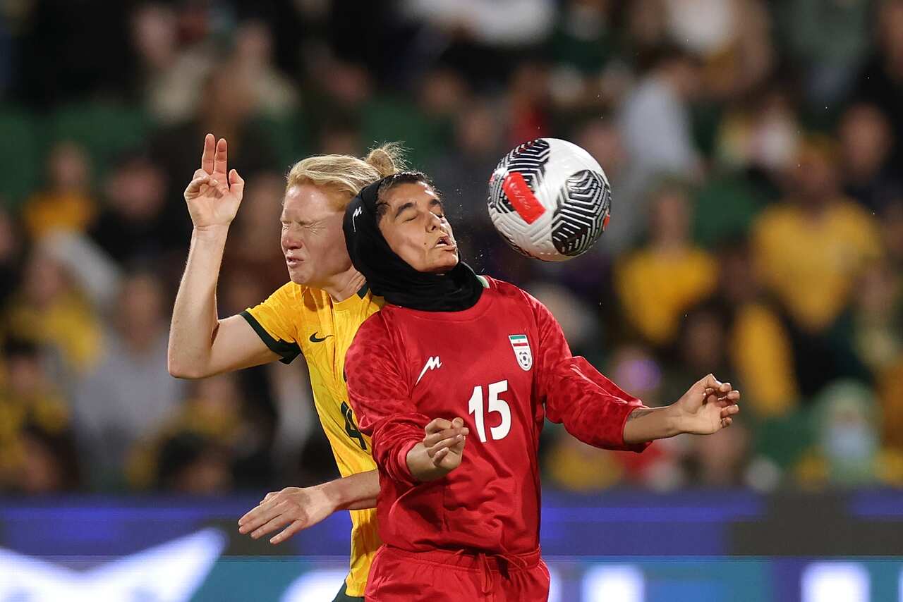 Two women in soccer uniforms leap for a ball