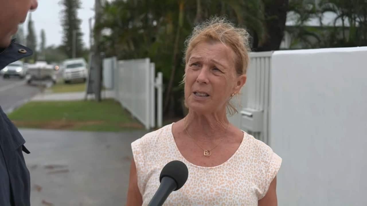 A woman standing outside her home and speaking to a journalist.