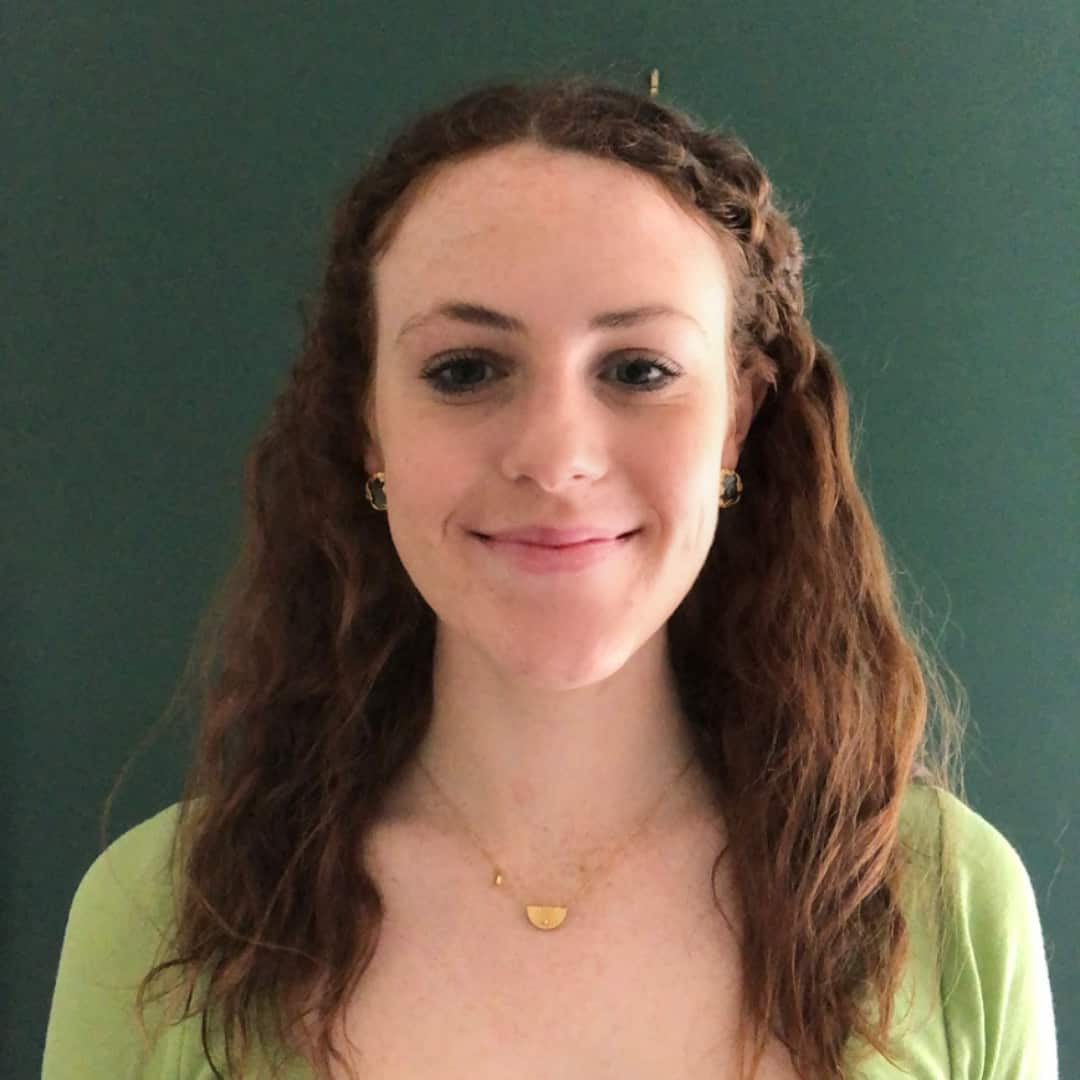 A girl in a green shirt smiles in front of a green wall. 