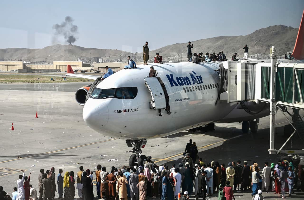 People crowding around a plane. Some are sitting on top of the aircraft.