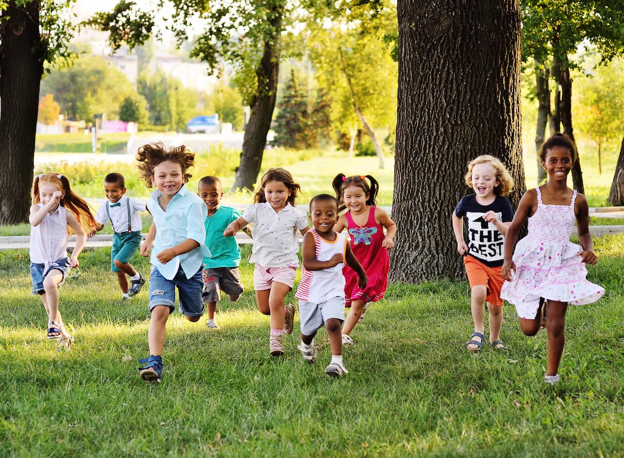 a group of preschoolers running on the grass in the Park