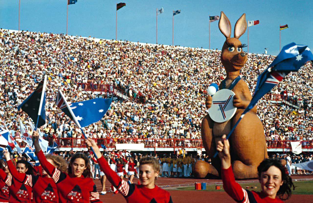 A giant kangaroo statue in a stadium full of people, with women in the foreground waving Australian flags.