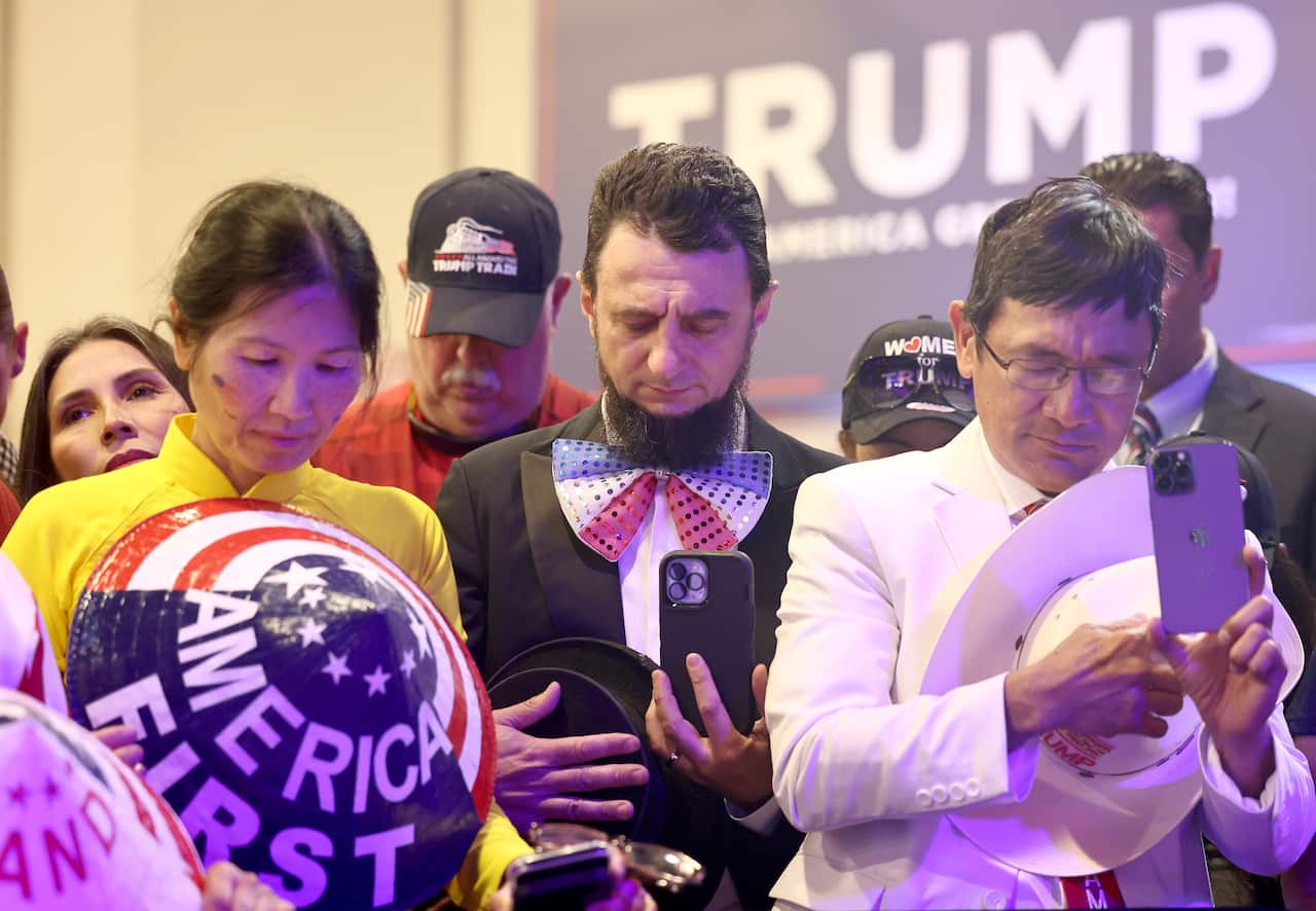 A group of people are standing, looking down at their mobile phones.