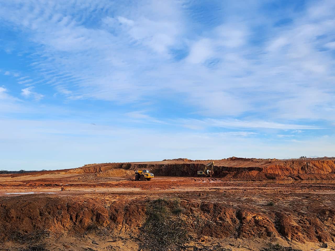 A large pit of red dirt with two earthmovers.