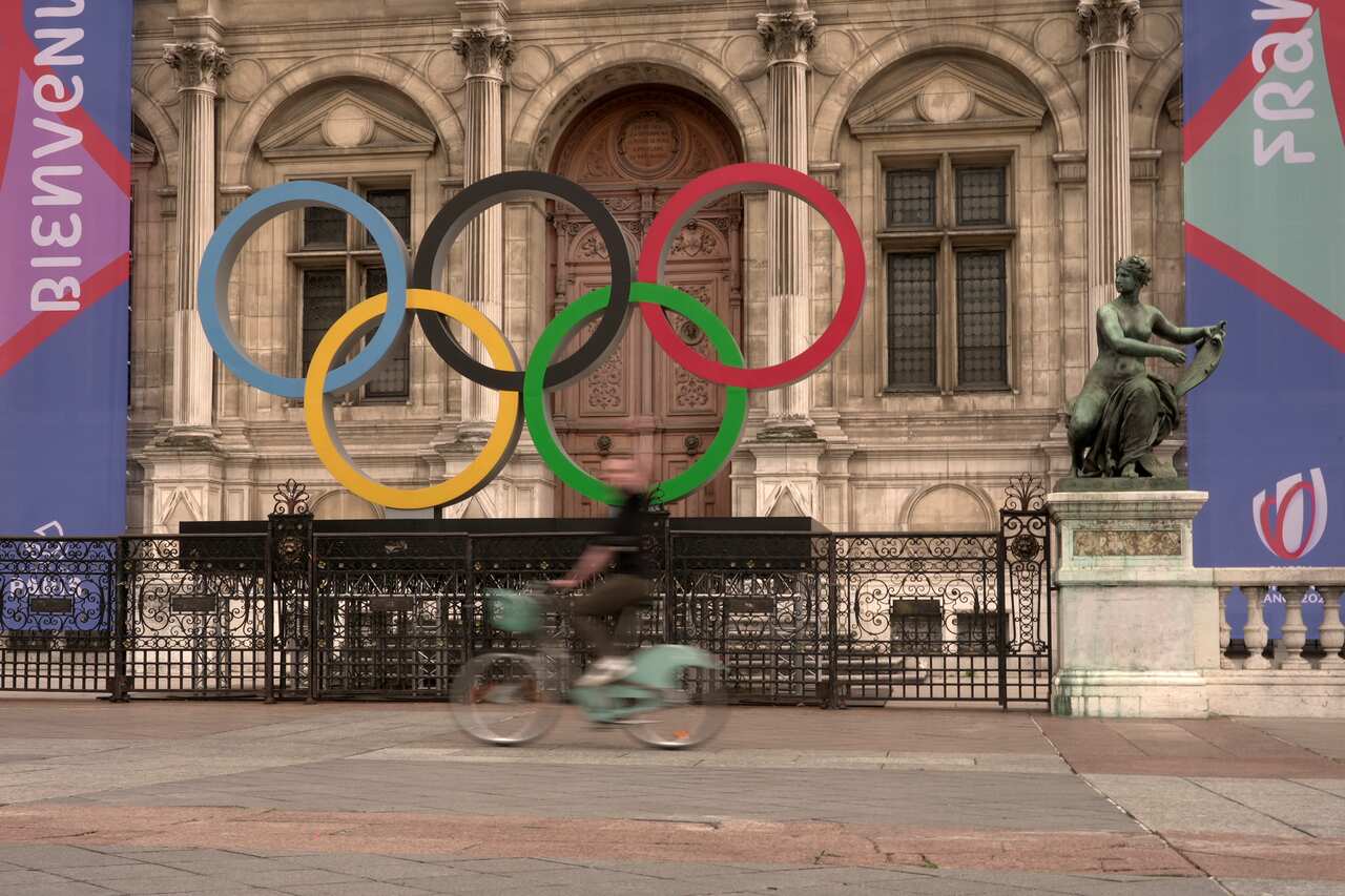 A person rides past the Olympic rings outside the Paris city hall.