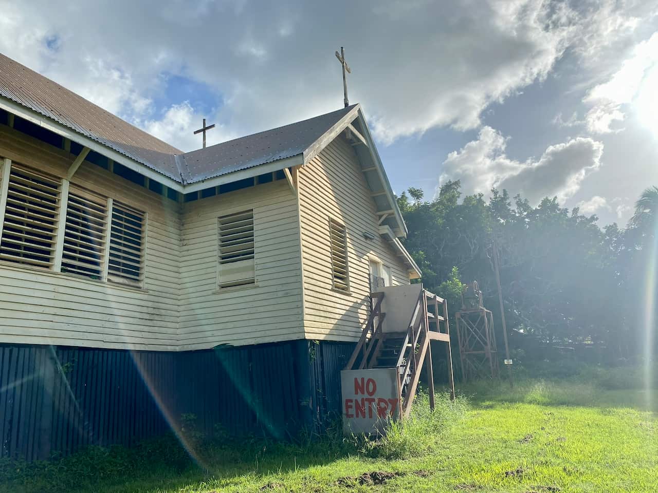 A timber-slatted church stands on stilts. A sign that reads ‘No Entry’ blocks the stairs.