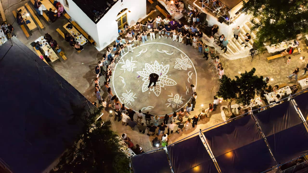An overhead shot of people gathering together in a circle around a painted mural on the floor. There are also tables of food and people eating.