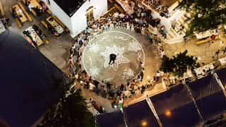 An overhead shot of people gathering together in a circle around a painted mural on the floor. There are also tables of food and people eating.