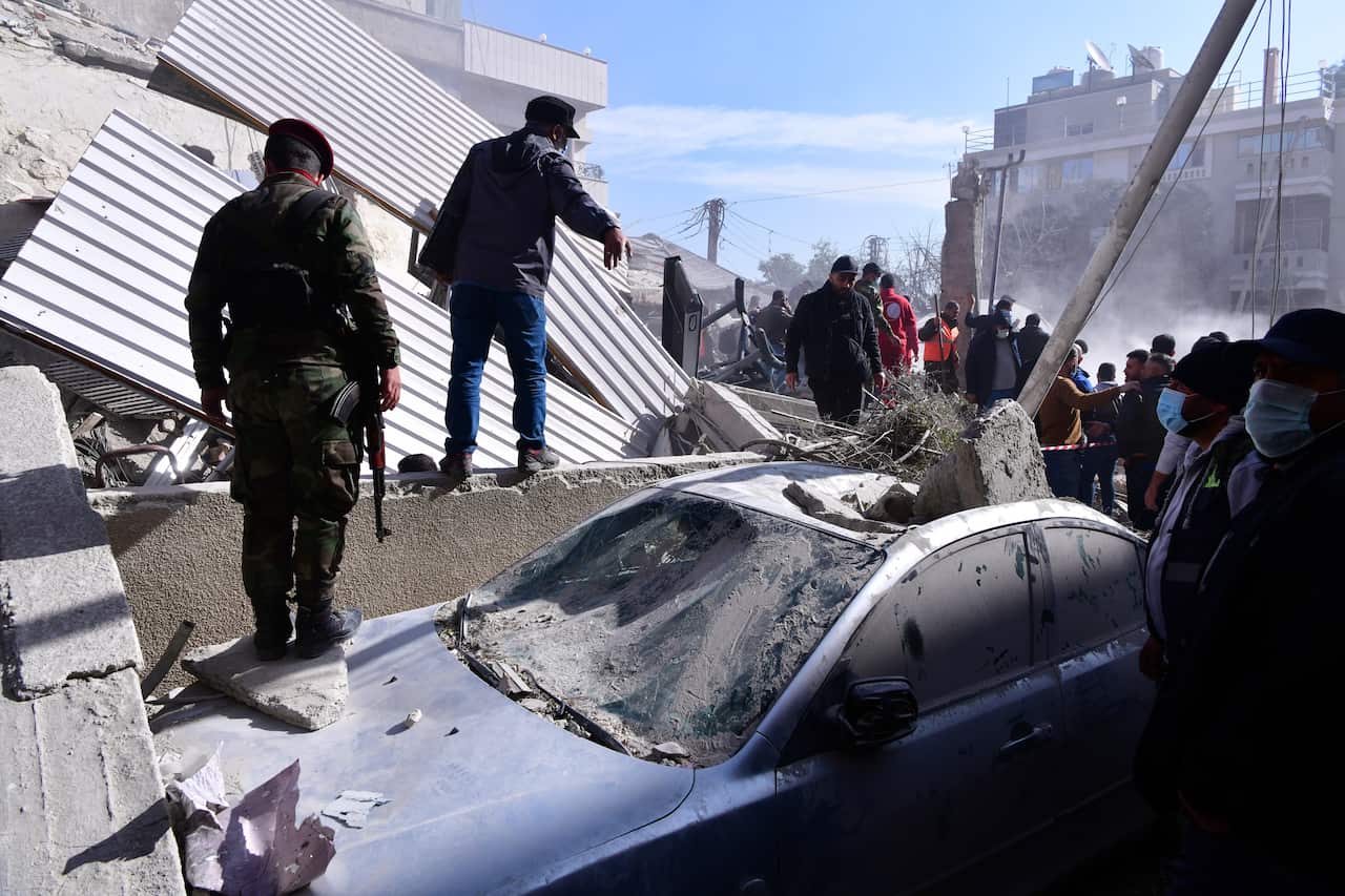 Soldiers inspecting damage and directing a group of people looking on.