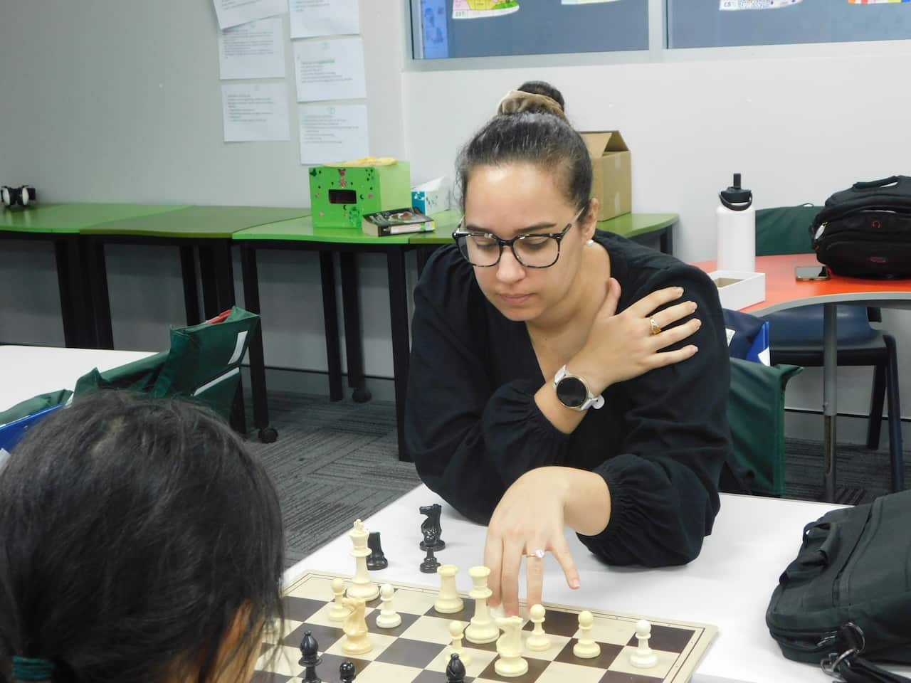 A woman teaching chess to a young girl in a classroom.