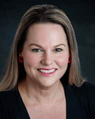 A woman in a black top with brown hair smiles at camera.