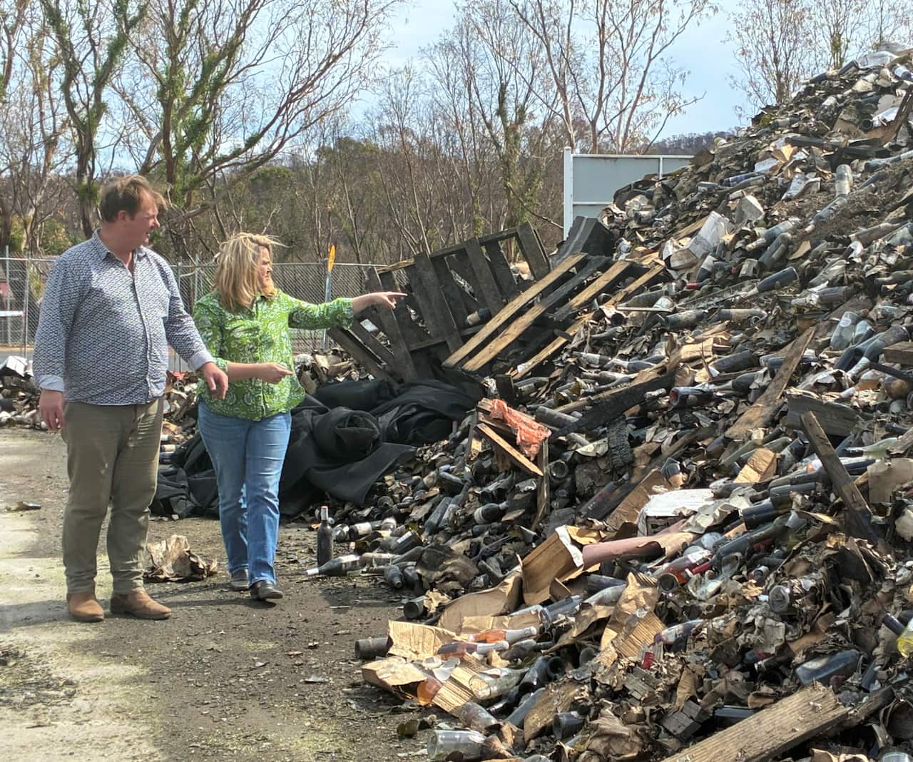 A couple stands next to a mound of debris, pointing to broken bottles.