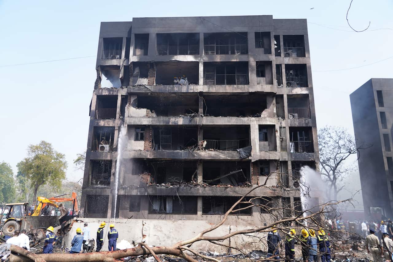 Rescue workers stand under a burnt and partially constructed building.