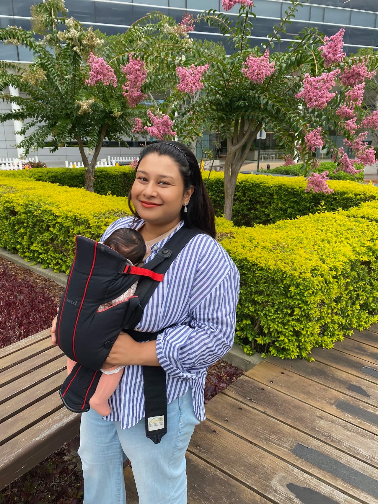 A woman smiles as she holds her baby, who lies in a carrier on her chest.