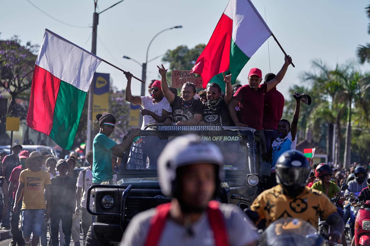 Protesters waving the Madagascar flag celebrate the back of a car. 