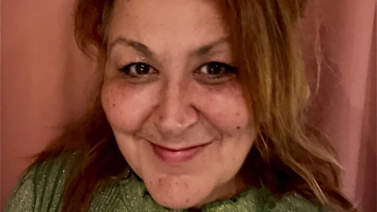 a close up shot of a woman with brown hair smiling in front of a pink background