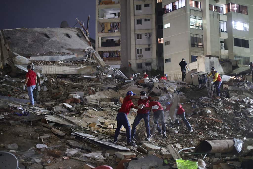 Workers wearing red shirts among the rubble of a collapsed building at night