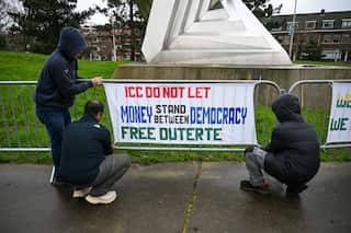 A group of people in black jackets attaches a protest sign to a temporary metal fence. The fence surrounds a triangular statue. The text of the poster reads: ICC DO NOT LET MONEY STAND BETWEN DEMOCRACY, FREE DUTERTE.