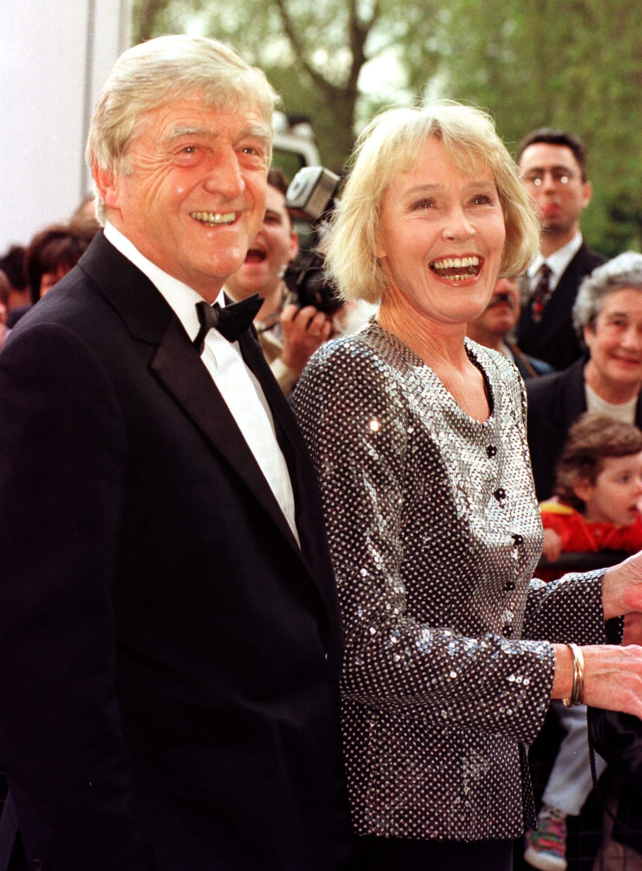 A man in a suit stands next to a woman as they both laugh.