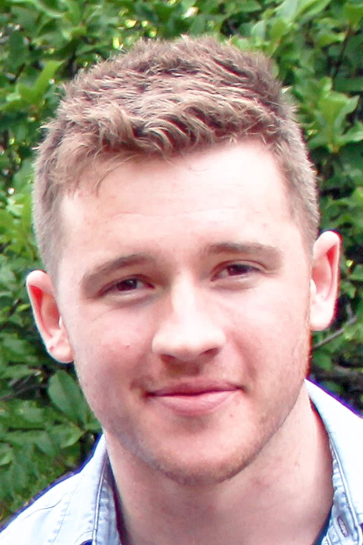 A portrait of a man smiling with some green foliage in the background.