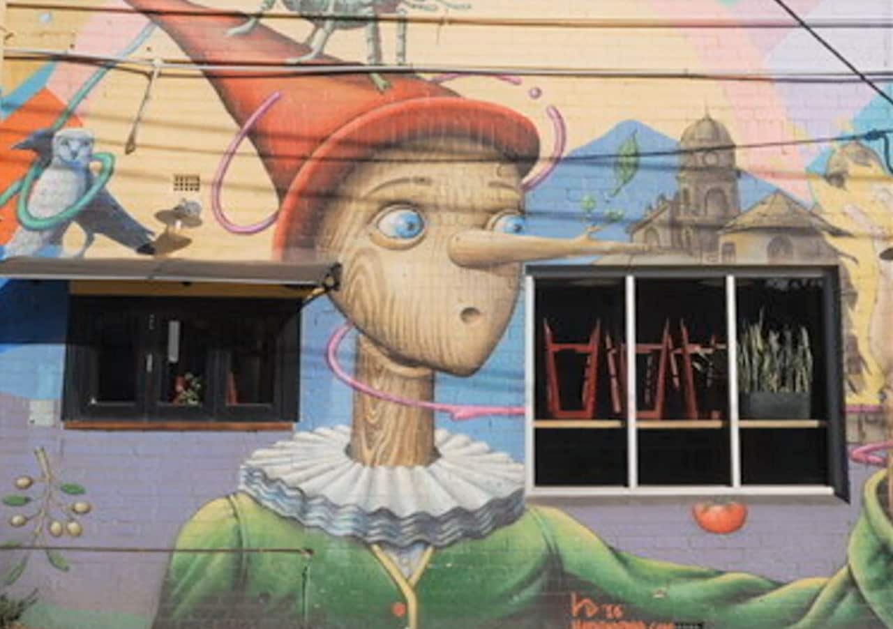 A street art painting of Pinocchio on a cafe exterior wall.