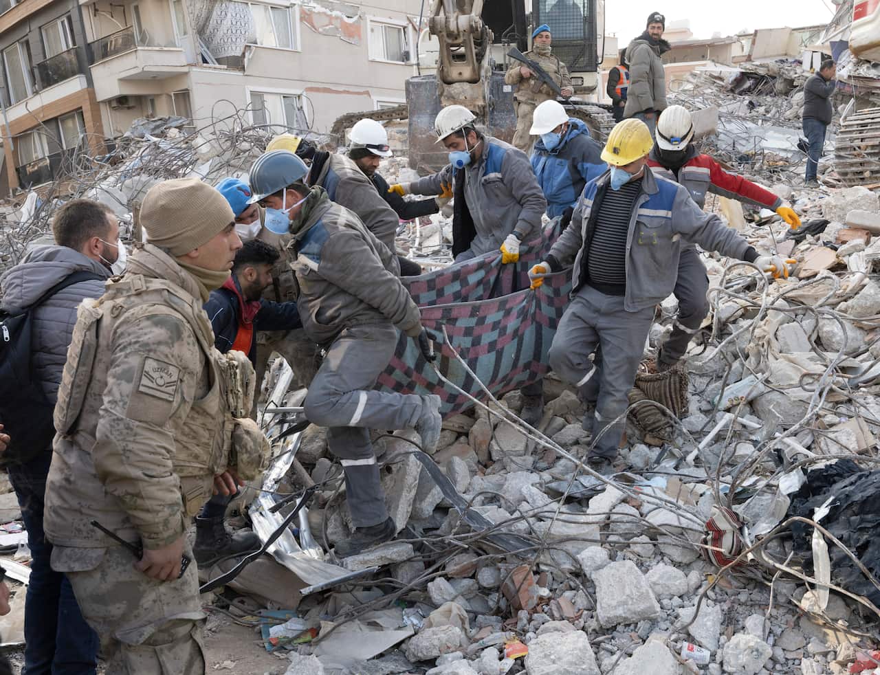 People in hardhats and face masks carry a blanket through earthquake rubble